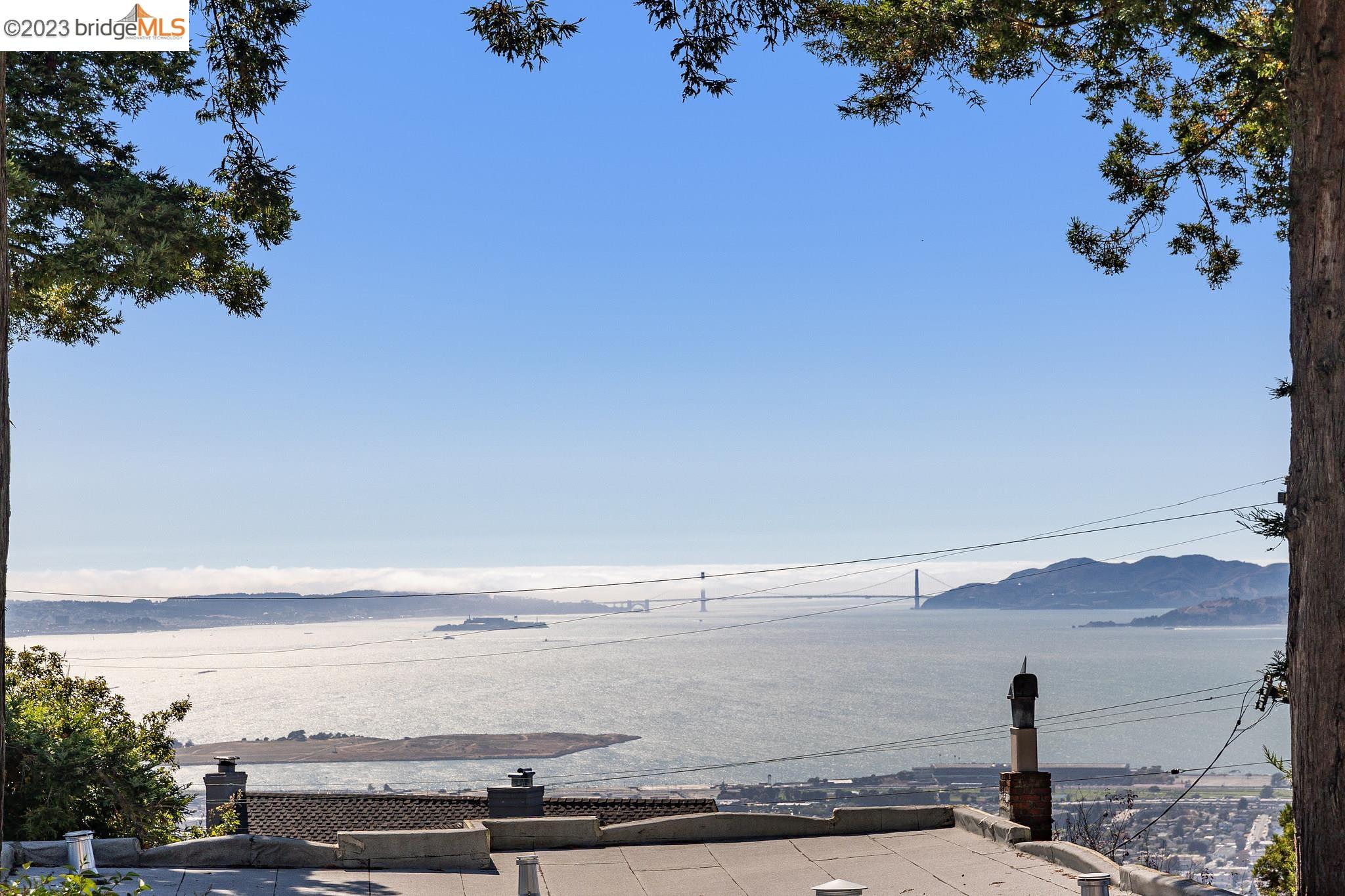 This elegant 1936 French Provincial frames world-class panoramic views of San Francisco city lights and three bridges; the Golden Gate, the Bay Bridge, and the Richmond Bridge. An entry courtyard, enclosed by a white picket fence, is adorned with stone pathways reminiscent of the French countryside. A soaring two-story foyer sets the tone for the grandeur within. French doors swing open to the patio, allowing guests to saunter naturally outside under the majestic magnolia tree. New west-facing Anderson windows frame captivating views of San Francisco, Alcatraz, Oakland, and Marin. Red oak flooring, wainscotting, and tongue-and-groove planks on the ceiling further embellish the stately rooms.  The views keep on giving in the kitchen breakfast room; a great space for an office or setting for smaller meals. A half bath off the entry hall adds convenience. A small mud room joins the kitchen to the garage which can easily be upgraded for electric vehicles.   Miraculously, all 3 upper bedrooms enjoy Bay views. The primary ensuite bathroom is adorned with Heath tile, features a walk-in closet, and spaciously accommodates a king-size bed. The lower level den is perfect for relaxed TV viewing, or an imaginative playroom for all ages. The 4th bedroom can be a private office or guest space.