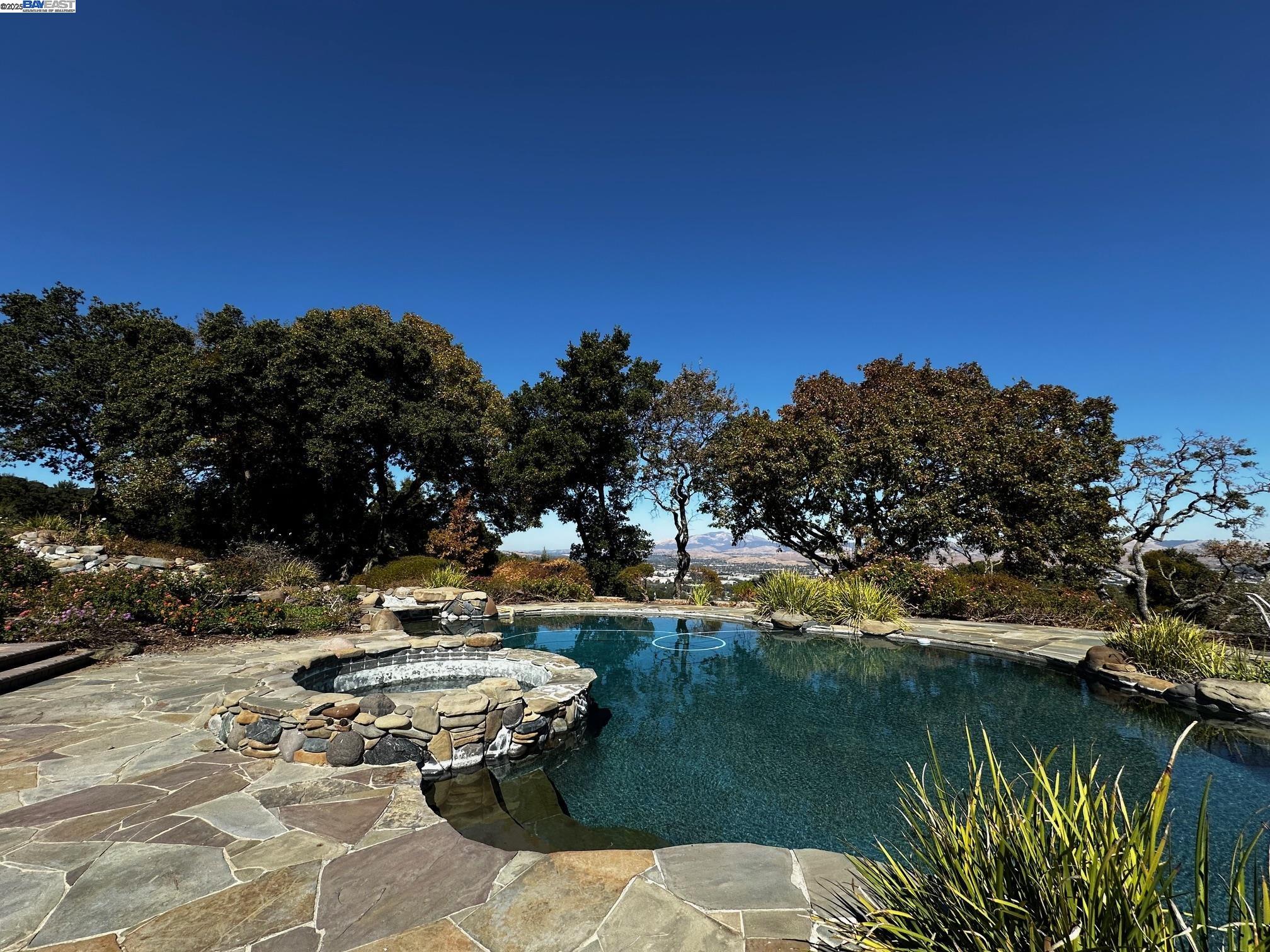 Nestled in the scenic Pleasanton Ridge, this 77.48-acre estate offers unmatched luxury and privacy. Built in 2000, the custom home spans 8,590 square feet with a single-level layout featuring seven bedrooms, six full baths, and two half baths. The gourmet kitchen is equipped with high-end appliances, stone countertops, and a breakfast bar, ideal for both everyday meals and entertaining. The adjacent family room boasts a cozy gas fireplace and large windows framing stunning views of Mt. Diablo and the valley. The expansive primary suite includes a spa-like bathroom with a jetted tub, stall shower, and skylight, plus a private retreat for quiet moments or a home office. A laundry room completes the main level. A highlight of this estate is the 10-car, museum-quality garage with heating, air conditioning, checkered flooring, and central vacuum. With 4 additional car garages provide extra storage and convenience. Outside, the landscaped grounds feature a swimming pool, a spacious deck, and a patio perfect for alfresco dining, all with panoramic views of the valley. This exceptional estate offers the ultimate in luxury, comfort, and natural beauty. Located in a top-rated school district, it provides excellent education for your children while offering a serene, outdoor lifestyle.