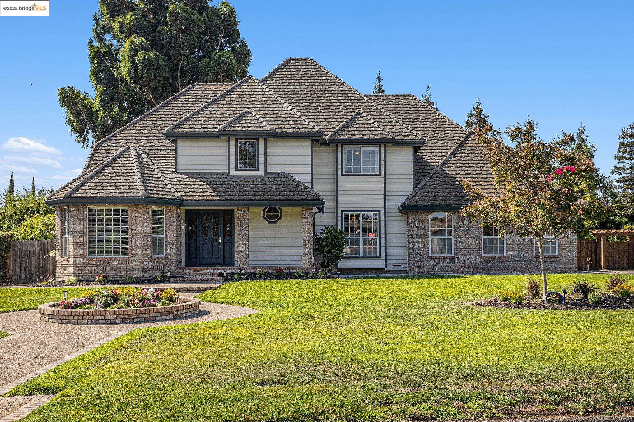 Prestigious Neroly Estates — A rare opportunity to own a nearly 1-acre custom estate framed by towering redwoods, mature magnolia, and crape myrtle with canal access for irrigation. Tucked away on a serene court of luxury homes, this property offers a private country feel with no streetlights or sidewalks, yet minutes to the Hwy 4 Bypass and Big Break Marina. A grand entry welcomes you into expansive living spaces featuring solid surface floors, a soaring floor-to-ceiling gas fireplace, and a sunroom retreat. The chef’s kitchen showcases a 48” Wolf gas range, prep island, trash compactor, dishwasher, and a pass-through to the formal dining room. The main-level primary suite is joined by a junior suite upstairs, plus two bedrooms with Jack-and-Jill bath and an office that can serve as a 5th bedroom. Every room features its own bathroom or shared ensuite, with deep walk-in closets throughout. Additional amenities include a hidden safe room (~100), enormous attic, epoxy-coated 3-car garage, basketball court, playground, fire pit, and expansive lawns perfect for entertaining. This estate blends privacy, luxury, and convenience — truly designed for the discerning Bay Area buyer.